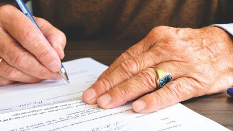 A senior signs documents with a pen